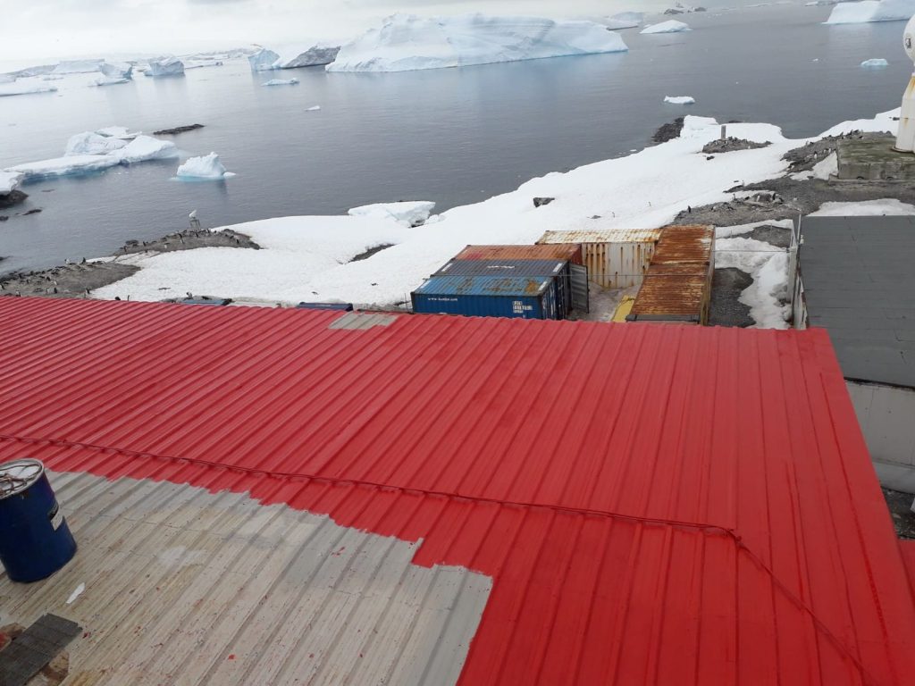 Techo metálico rojo terminado con membrana de poliurea en la Antártica, rodeado de nieve